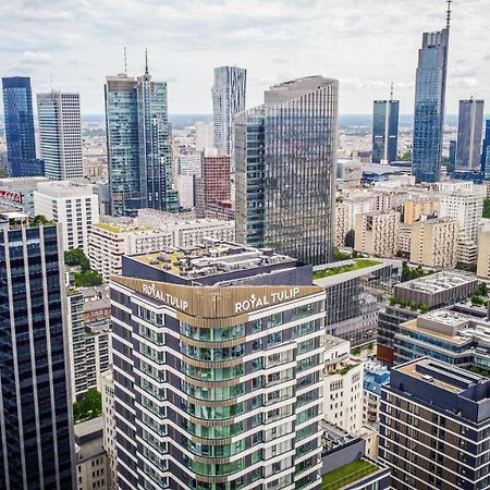 Aparthotel Royal Tulip Warsaw Centre Exterior foto The photo shows a panoramic view of a modern city skyline. In the foreground, there are several tall buildings with contemporary architectural designs. One building prominently features the name "Royal Tulip." The background is filled with numerous s