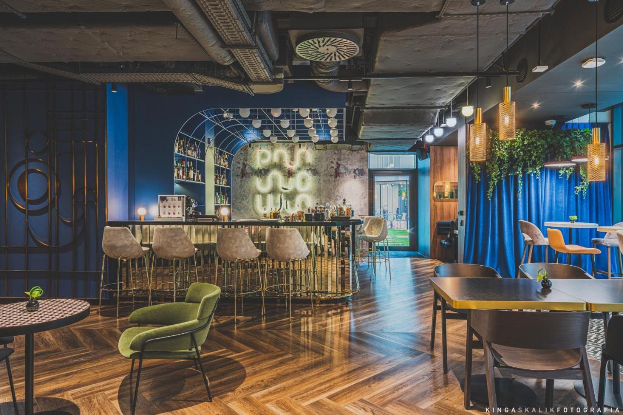 Aparthotel Royal Tulip Warsaw Centre Exterior foto The photo shows a modern and stylish bar or lounge area. It features a curved, elegant bar with high stools arranged in front. Behind the bar, there is a wall with mixed materials, partially illuminated, which likely showcases a selection of drinks. 