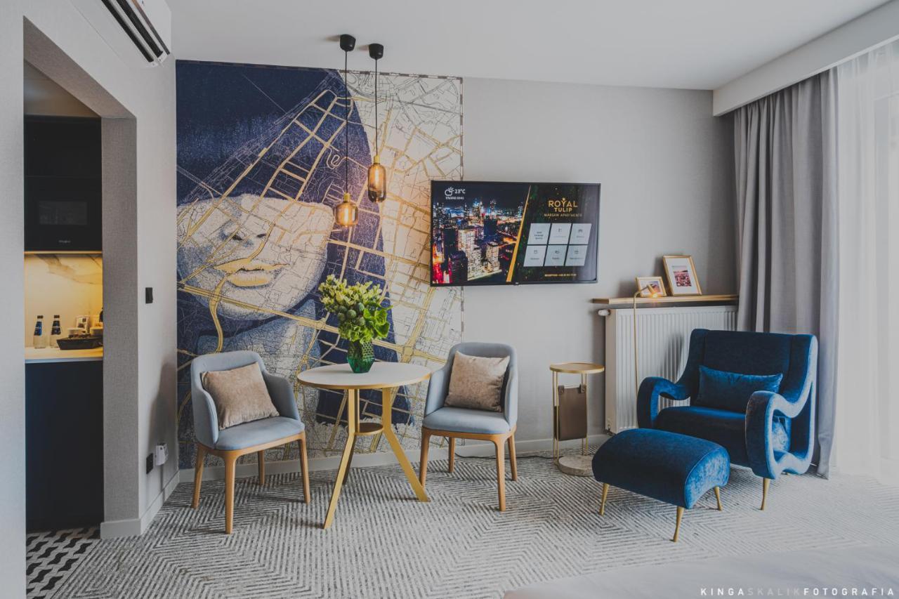 Aparthotel Royal Tulip Warsaw Centre Exterior foto The photo shows a modern living space featuring a stylish interior design. There is a mural on the wall that depicts a face with an abstract background. In the center of the room, there is a small round table surrounded by four chairs. A vase with fl