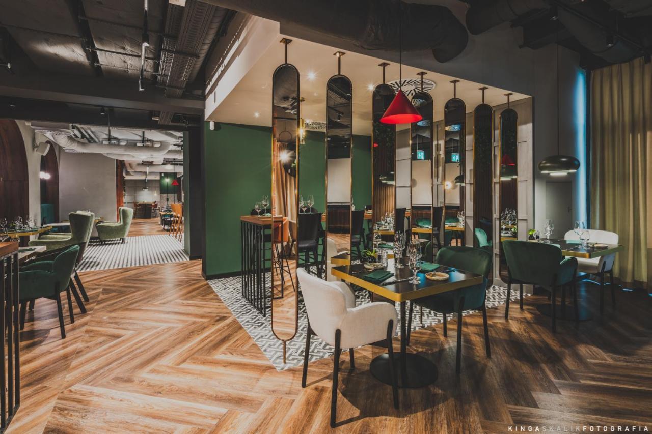 Aparthotel Royal Tulip Warsaw Centre Exterior foto The image depicts a modern restaurant interior. It features a combination of stylish furniture, including green and white chairs around wooden tables. The floor has a distinctive herringbone pattern, and there are mirrors along the walls, adding dept