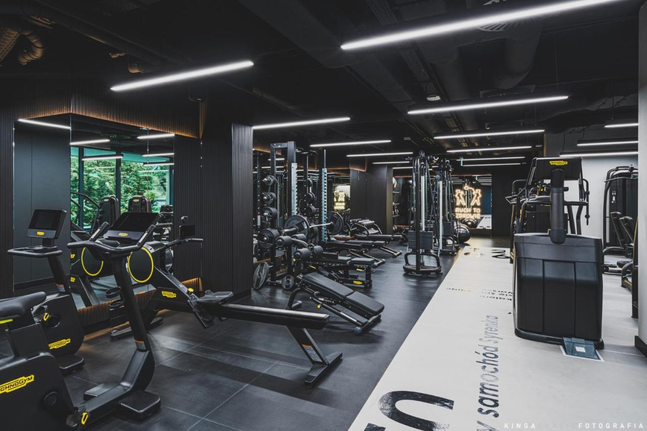 Aparthotel Royal Tulip Warsaw Centre Exterior foto The photo shows a modern gym interior with a sleek design. It features a variety of exercise equipment, including weight machines, free weights, and cardio machines. The space is well-lit with overhead lighting, and there are large windows allowing n