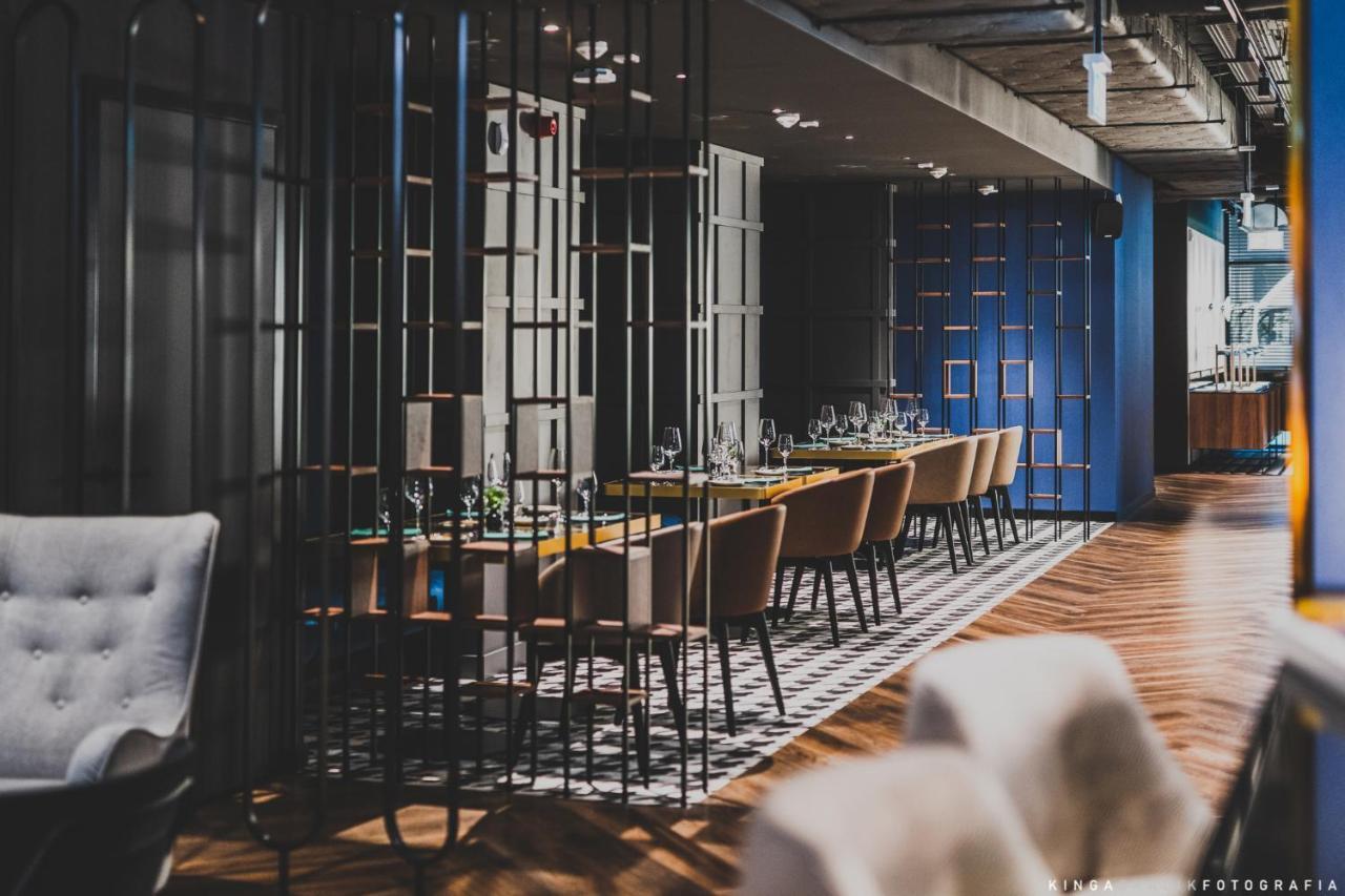 Aparthotel Royal Tulip Warsaw Centre Exterior foto The photo shows a modern restaurant interior. There are multiple dining tables arranged in a long line, each set with tableware and glassware. The space is divided by decorative metal partitions, creating an intimate atmosphere. The flooring features