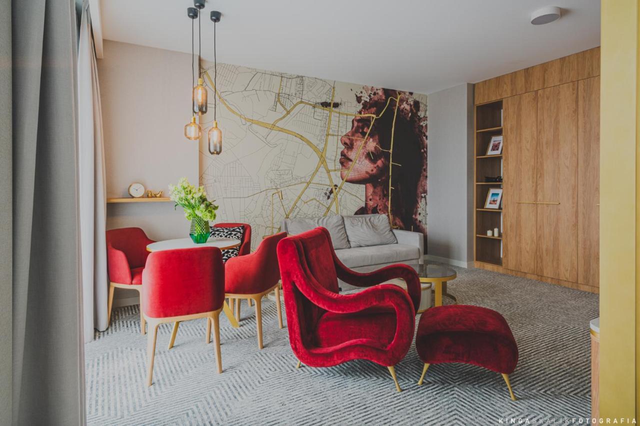 Aparthotel Royal Tulip Warsaw Centre Exterior foto The photo shows a stylish and modern living space. The room features a large wall mural depicting a woman's face, which adds an artistic touch. In the foreground, there are several red armchairs with a plush design, complemented by a small round tabl