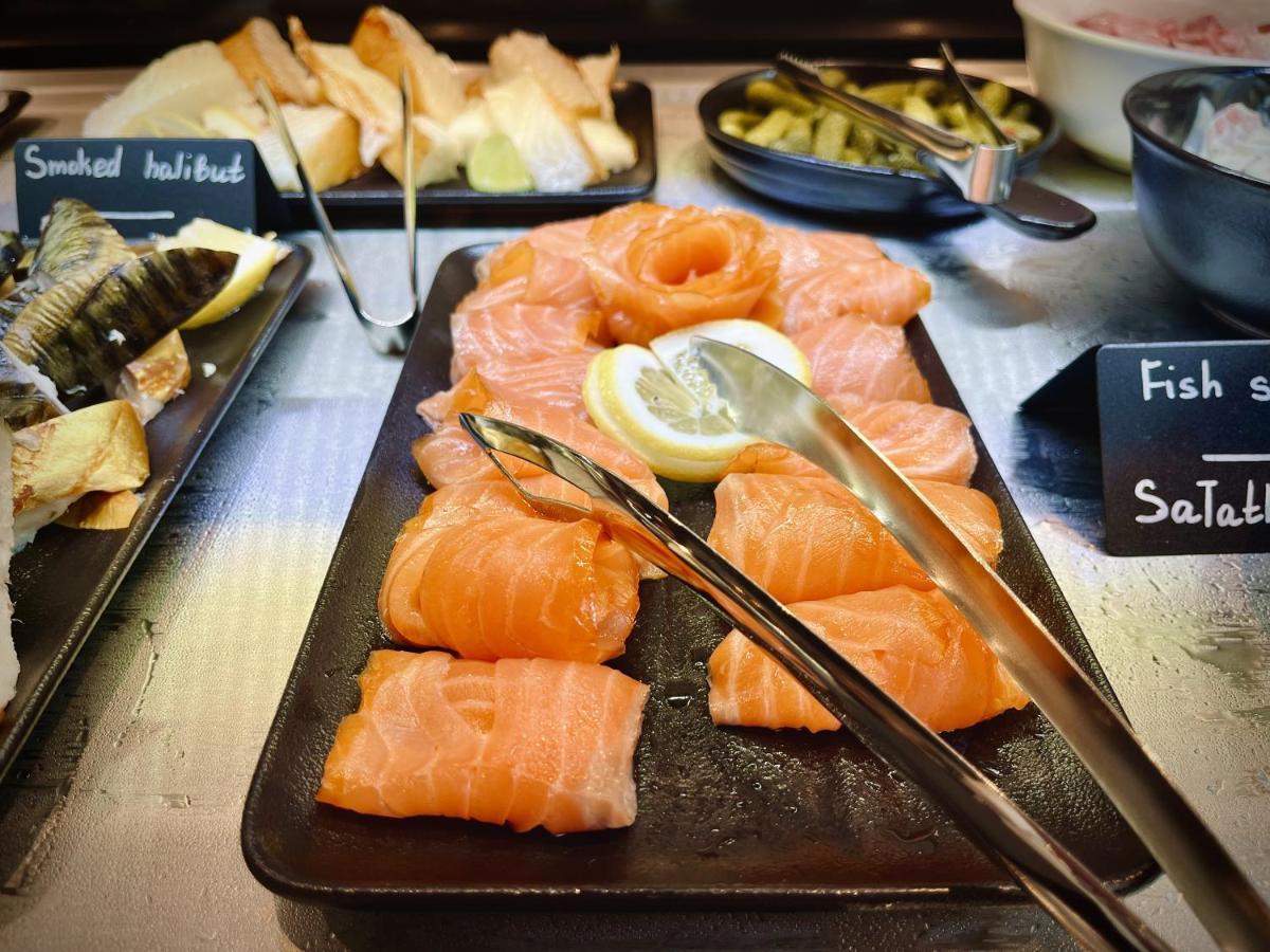 Aparthotel Royal Tulip Warsaw Centre Exterior foto The photo displays a variety of food items arranged on a serving platter. Prominently featured are slices of smoked salmon, some garnished with a lemon slice. There are also small labels indicating different types of fish, and nearby, other items suc