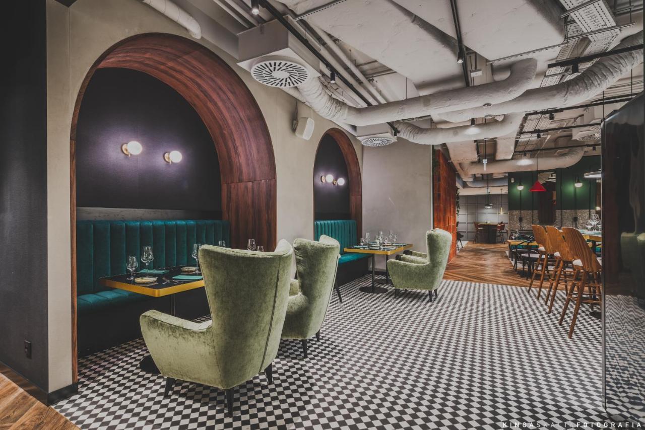 Aparthotel Royal Tulip Warsaw Centre Exterior foto The photo shows a stylish restaurant interior. It features arched openings with warm wood accents and green upholstered seating. The seating includes plush, green armchairs arranged around tables, creating a cozy atmosphere. The floor is decorated wi