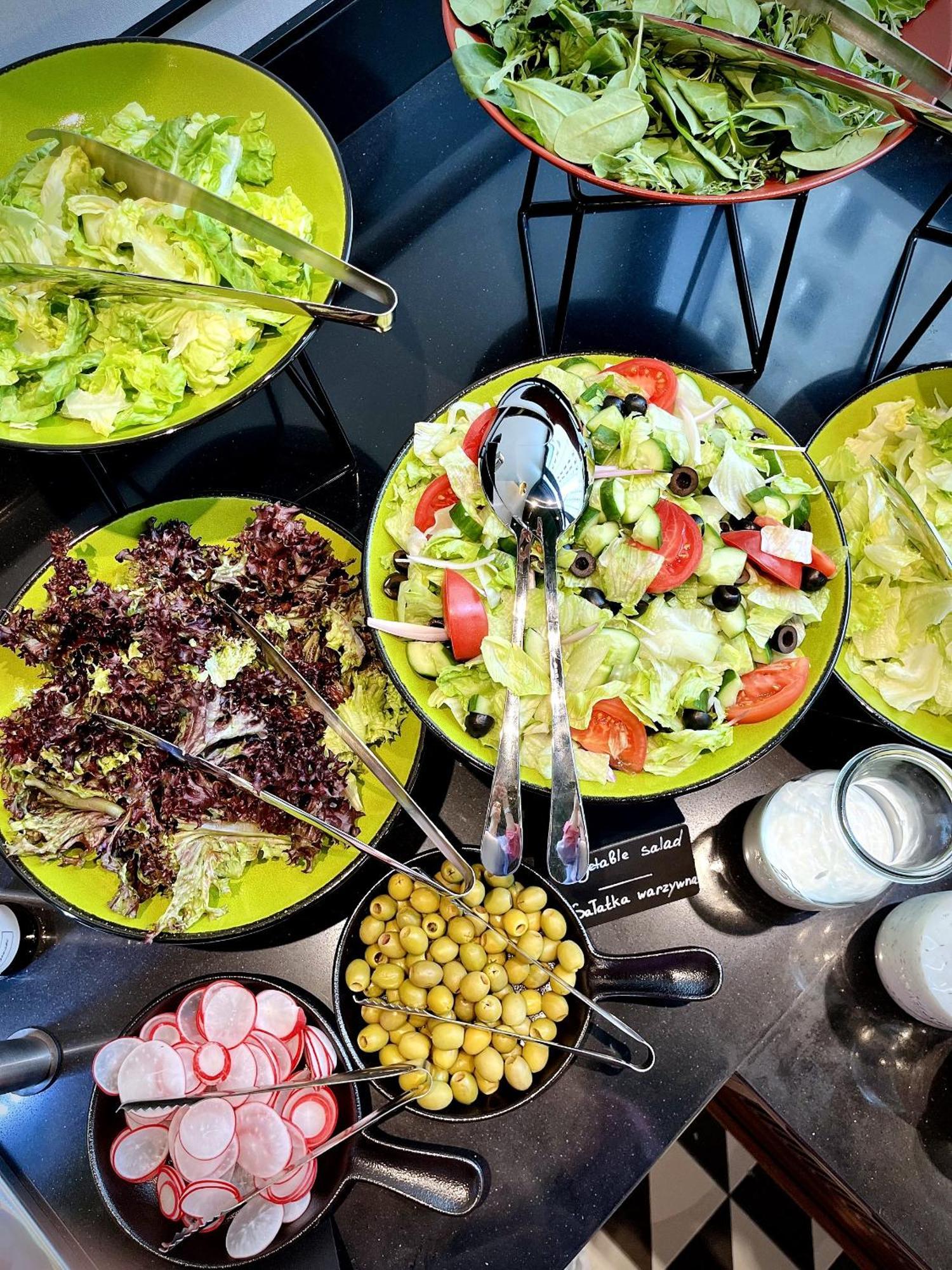 Aparthotel Royal Tulip Warsaw Centre Exterior foto The photo shows a variety of salads displayed in bowls. There are two main salad bowls:

1. **Left Bowl**: Contains dark leafy greens, possibly a mix of different kinds of lettuce or salad greens.
  
2. **Right Bowl**: Features a colorful salad with 