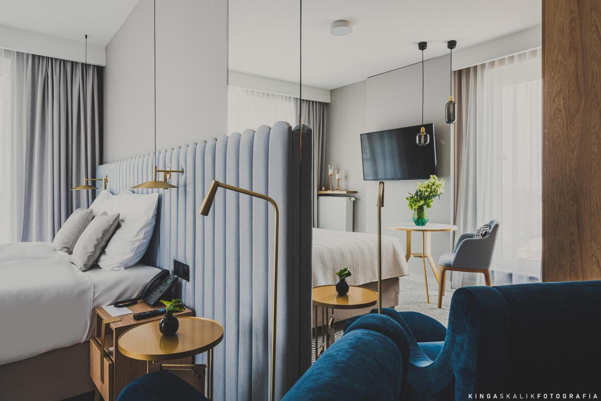 Aparthotel Royal Tulip Warsaw Centre Exterior foto The photo shows a modern hotel room featuring a stylish and contemporary design. In the foreground, there is a bed with a plush, upholstered headboard and white bedding. Beside the bed, there are sleek wooden bedside tables with small plants on top.
