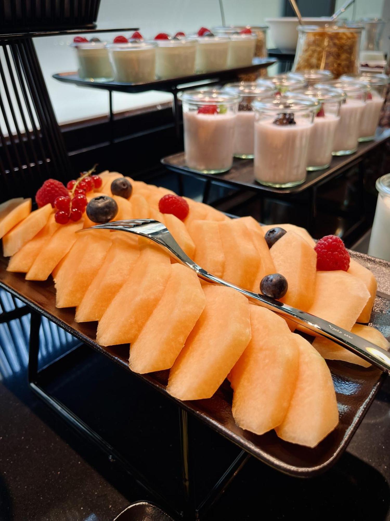 Aparthotel Royal Tulip Warsaw Centre Exterior foto The photo features a platter of sliced cantaloupe, arranged neatly and garnished with a few berries. There are red raspberries and blueberries placed on top of the melon slices. In the background, there are cups of dessert, likely some type of puddin