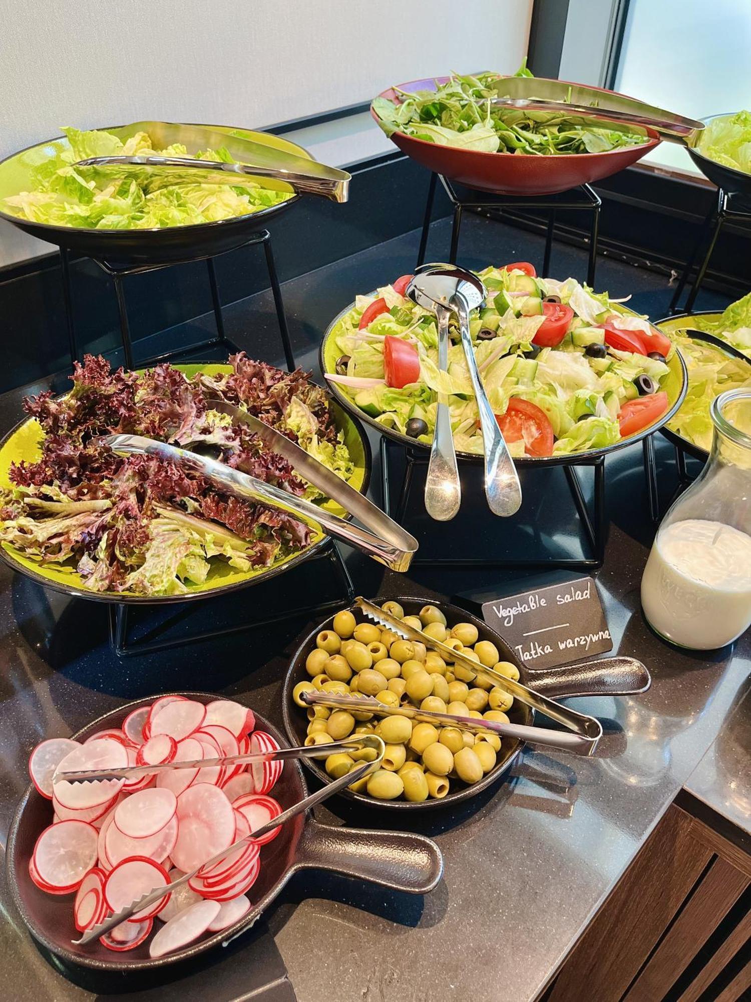 Aparthotel Royal Tulip Warsaw Centre Exterior foto The photo shows a variety of salad options arranged on a table. 

1. **Salads**: There are two larger bowls—one with mixed greens, including red leaf lettuce, and another with a colorful salad that includes chopped tomatoes, cucumbers, and olives.
2.