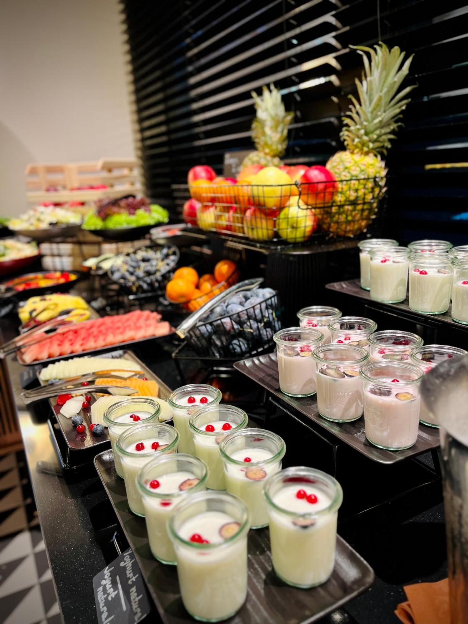 Aparthotel Royal Tulip Warsaw Centre Exterior foto The photo displays an assortment of food items arranged on a buffet table. In the foreground, there are several small glass containers filled with creamy desserts, garnished with red berries. Behind them, various fruits are presented, including apple