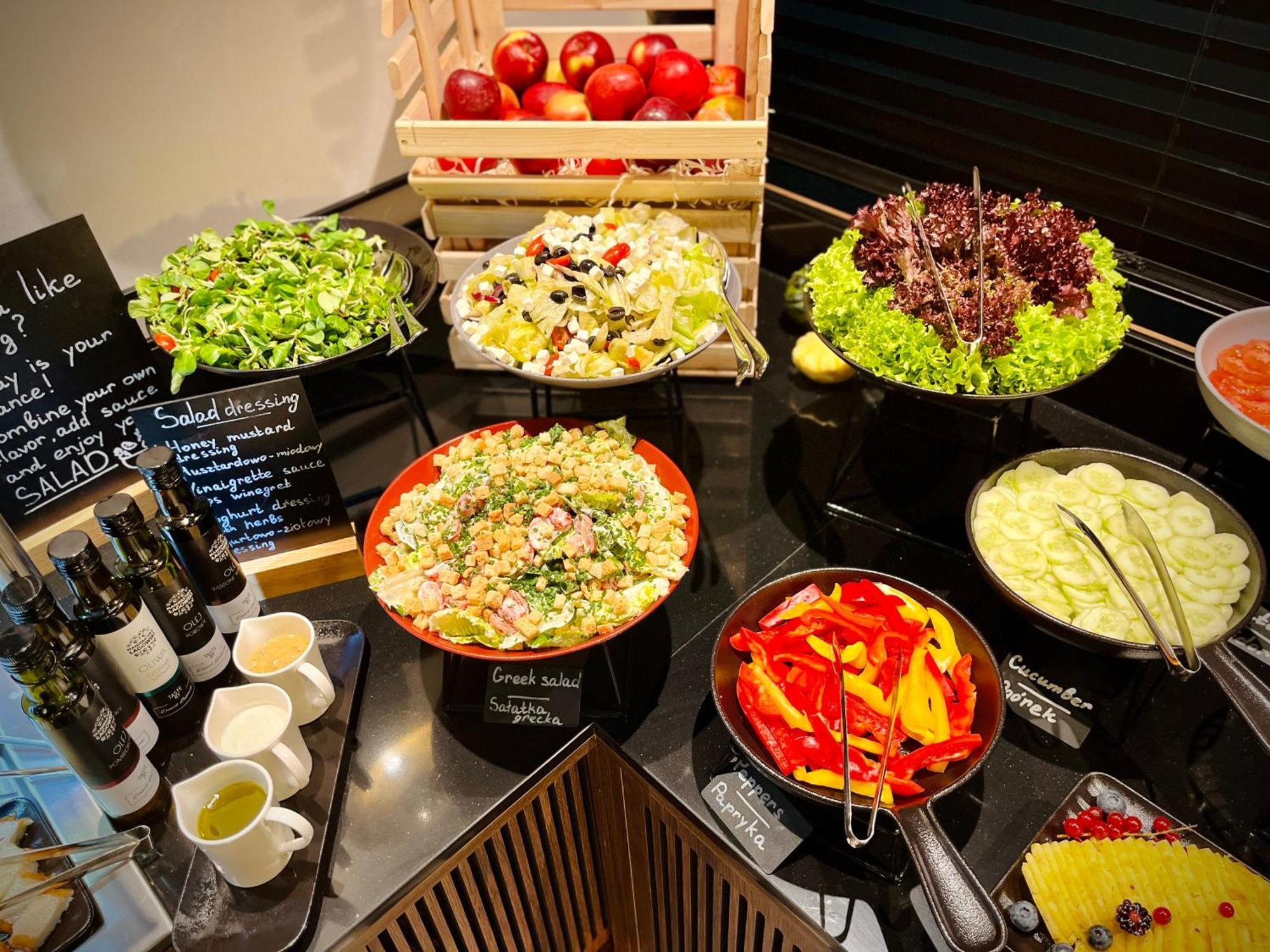 Aparthotel Royal Tulip Warsaw Centre Exterior foto The photo shows a well-arranged salad bar featuring a variety of fresh salads and ingredients. There are several bowls and dishes with different types of salads, including green salads and grain salads. 

1. **Green Salads**: There are multiple bowls